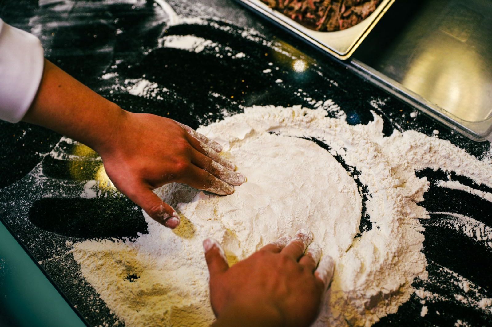 Hands folding fresh pasta dough into flour on a steel counter