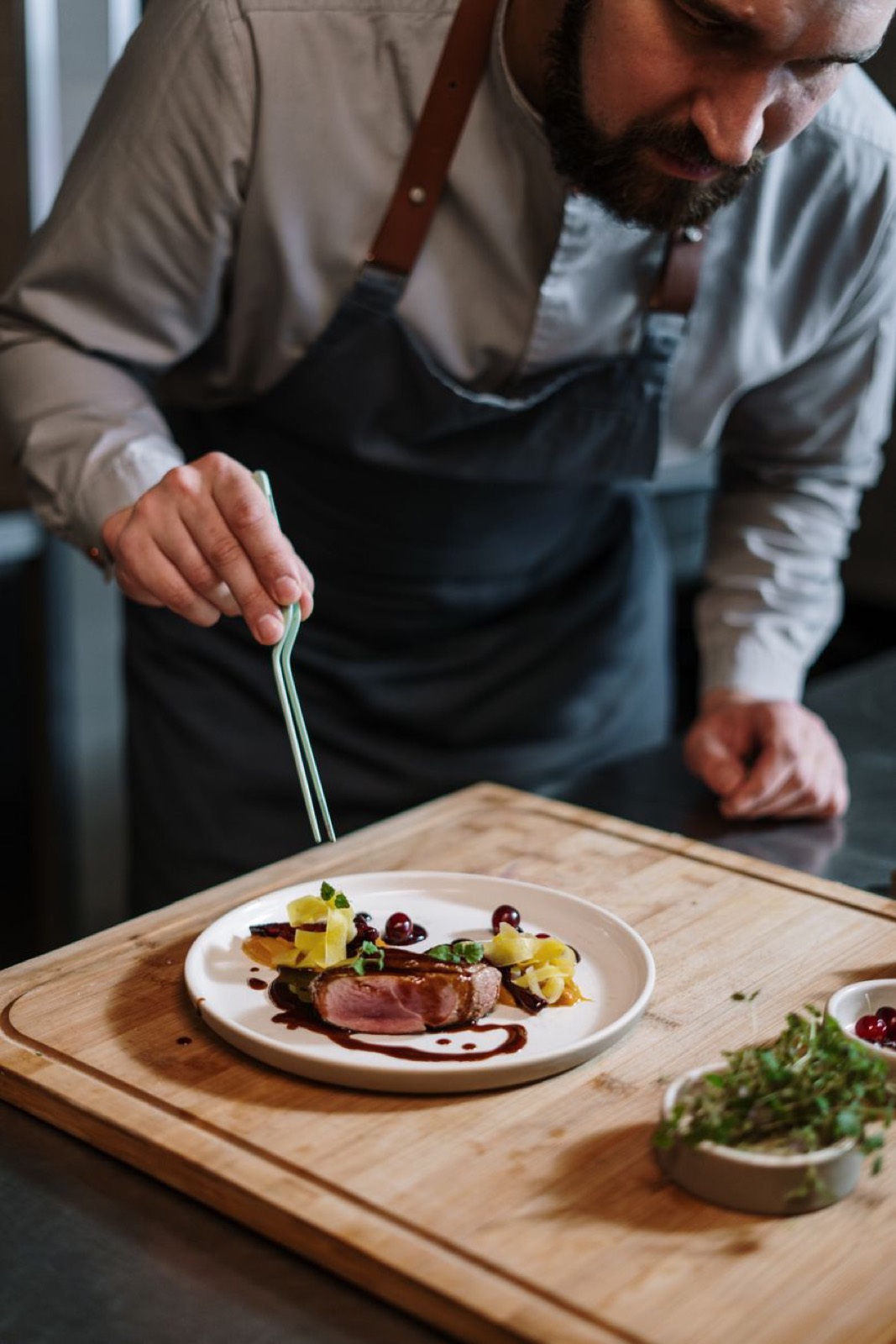 A chef plating with tweezers on a wooden board