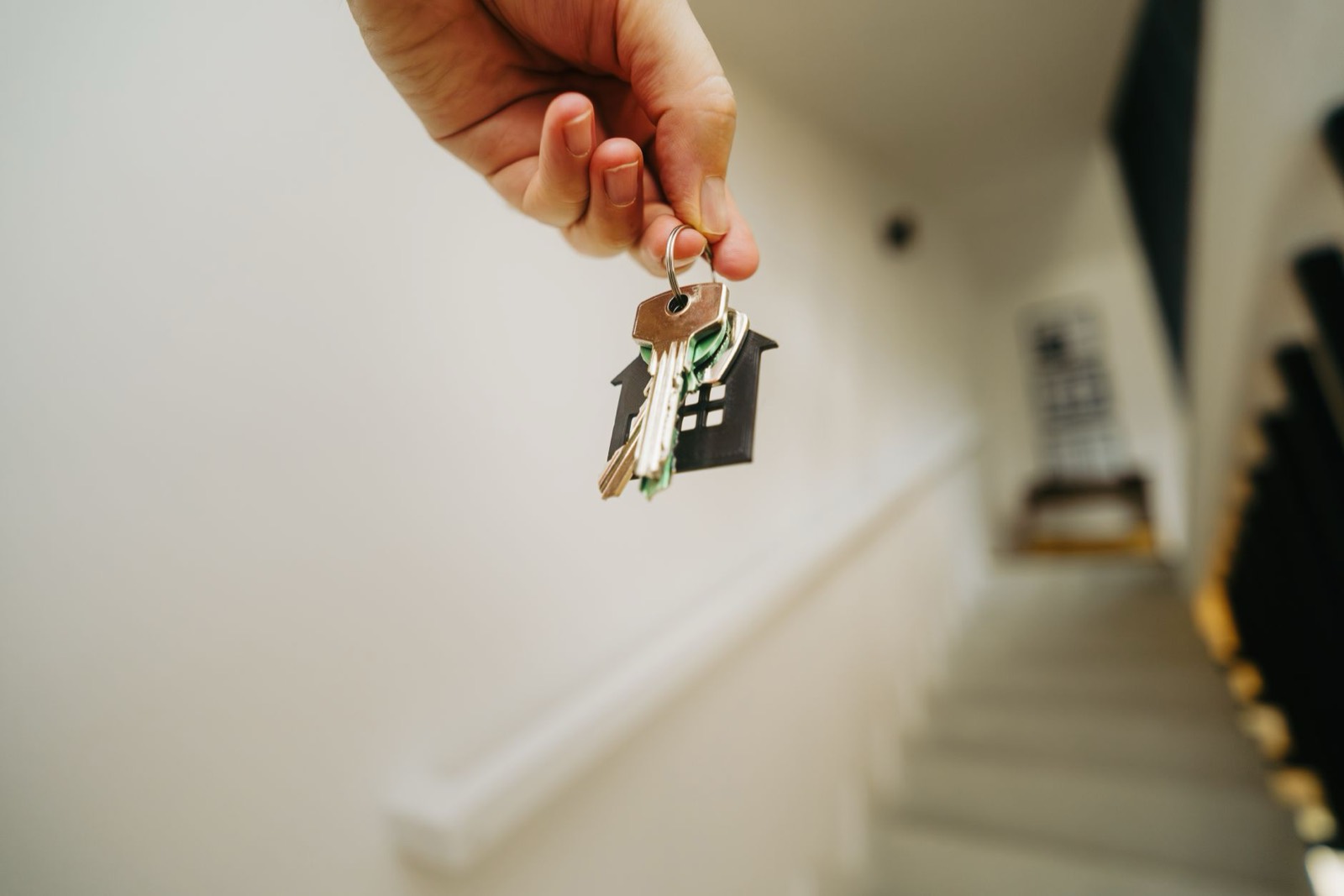 A hand holding house keys with a wooden house keyring