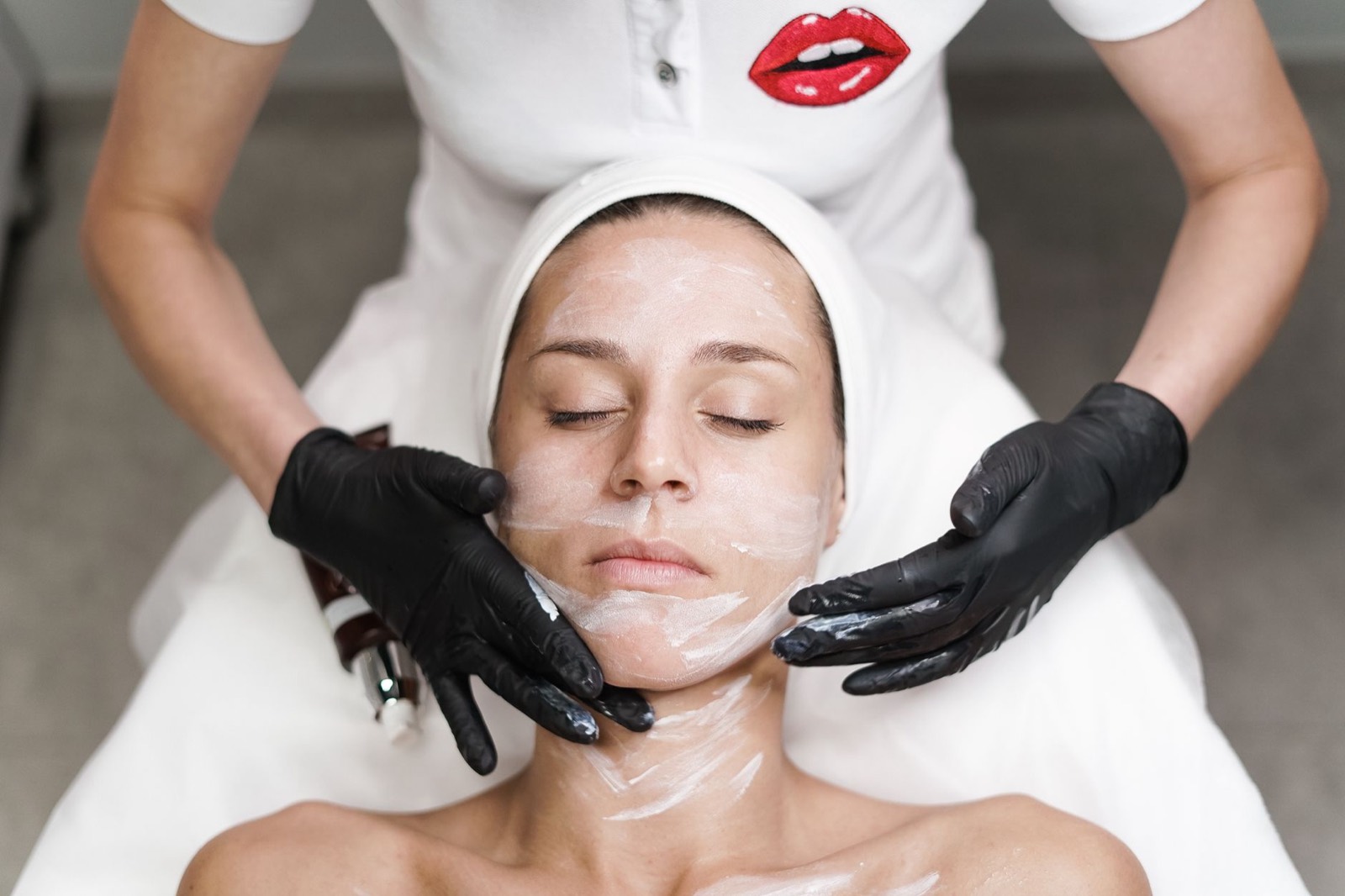 A client with eyes closed during a facial, the therapist's gloved hands at her cheeks