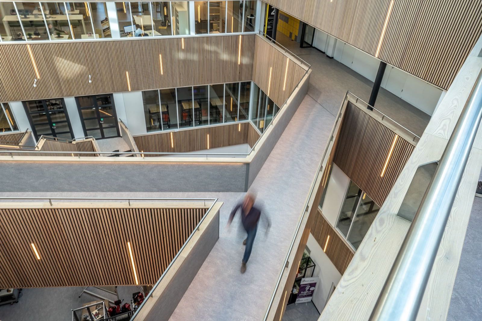A timber-lined atrium with a bridge, one person crossing