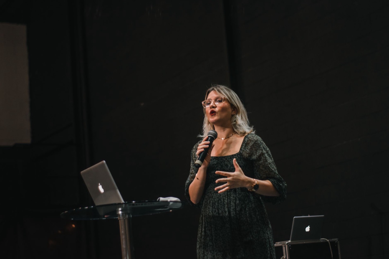Nina speaking on a dark stage with a microphone