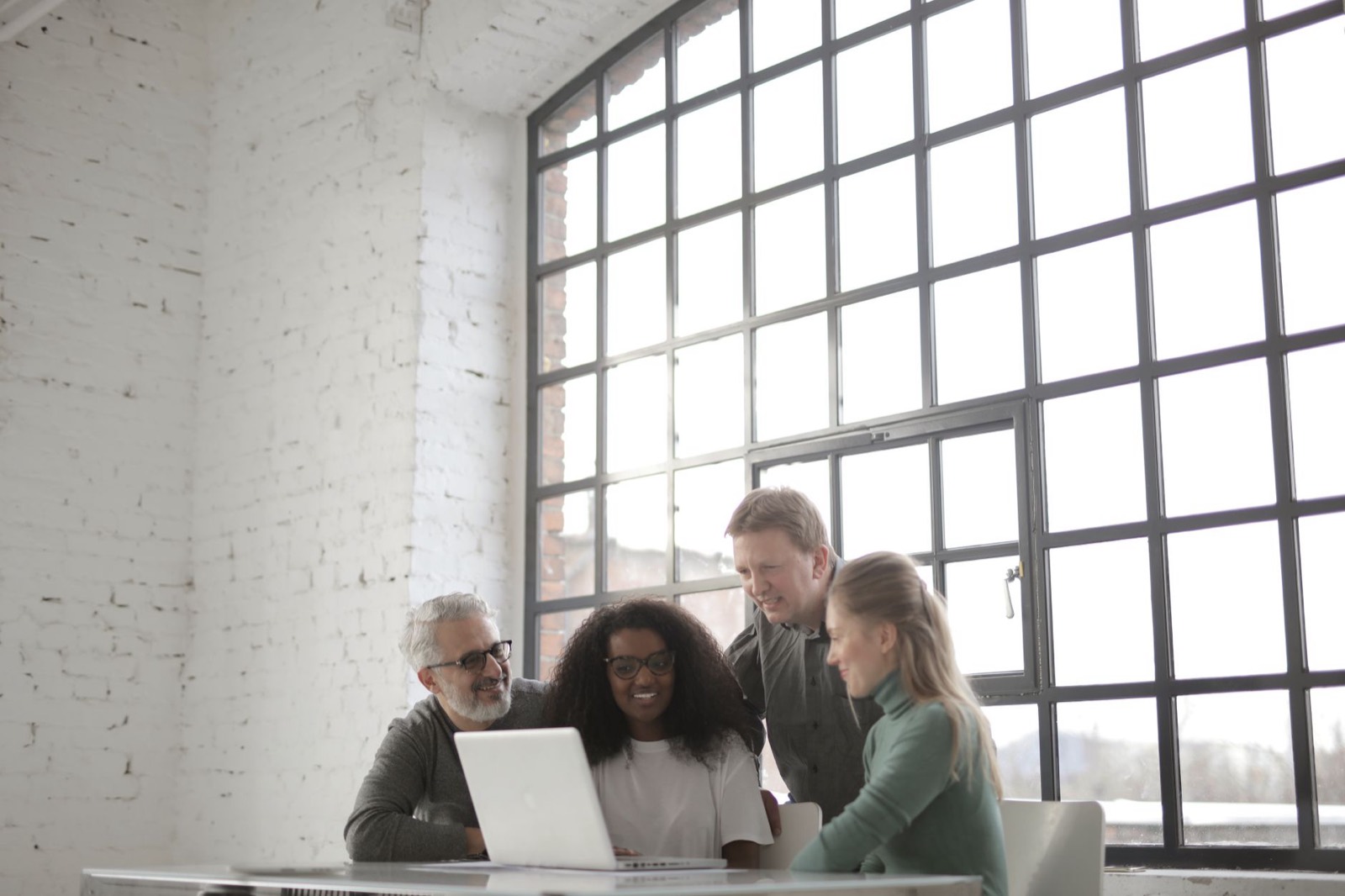Four colleagues around a laptop by a tall factory window