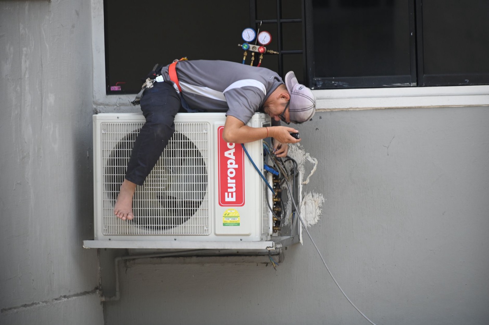 A technician leaning over an air-conditioning unit on an outside wall