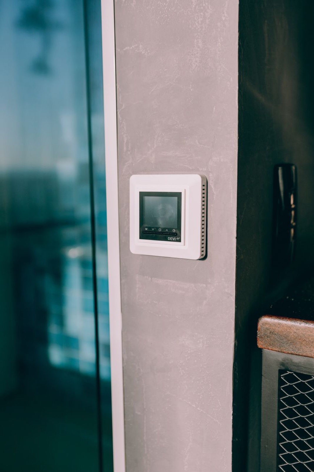 A white smart thermostat on a grey wall