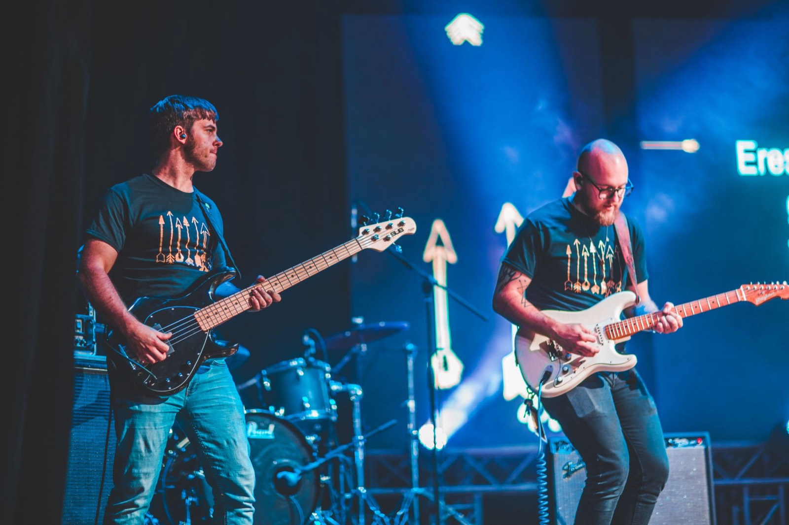 Two guitarists mid-song under blue stage light