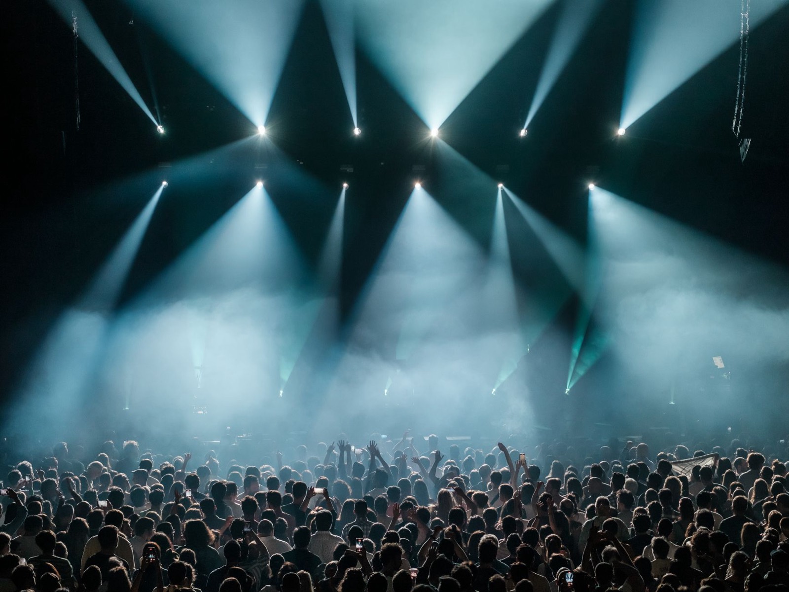 A festival crowd under fans of white stage light