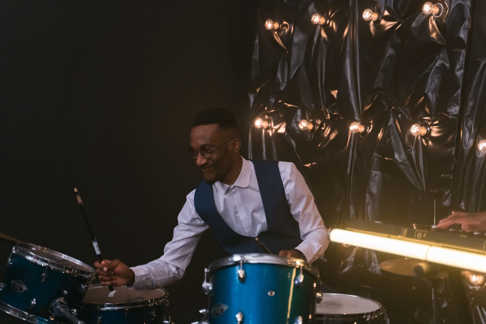 The drummer at a blue kit, smiling, sticks up