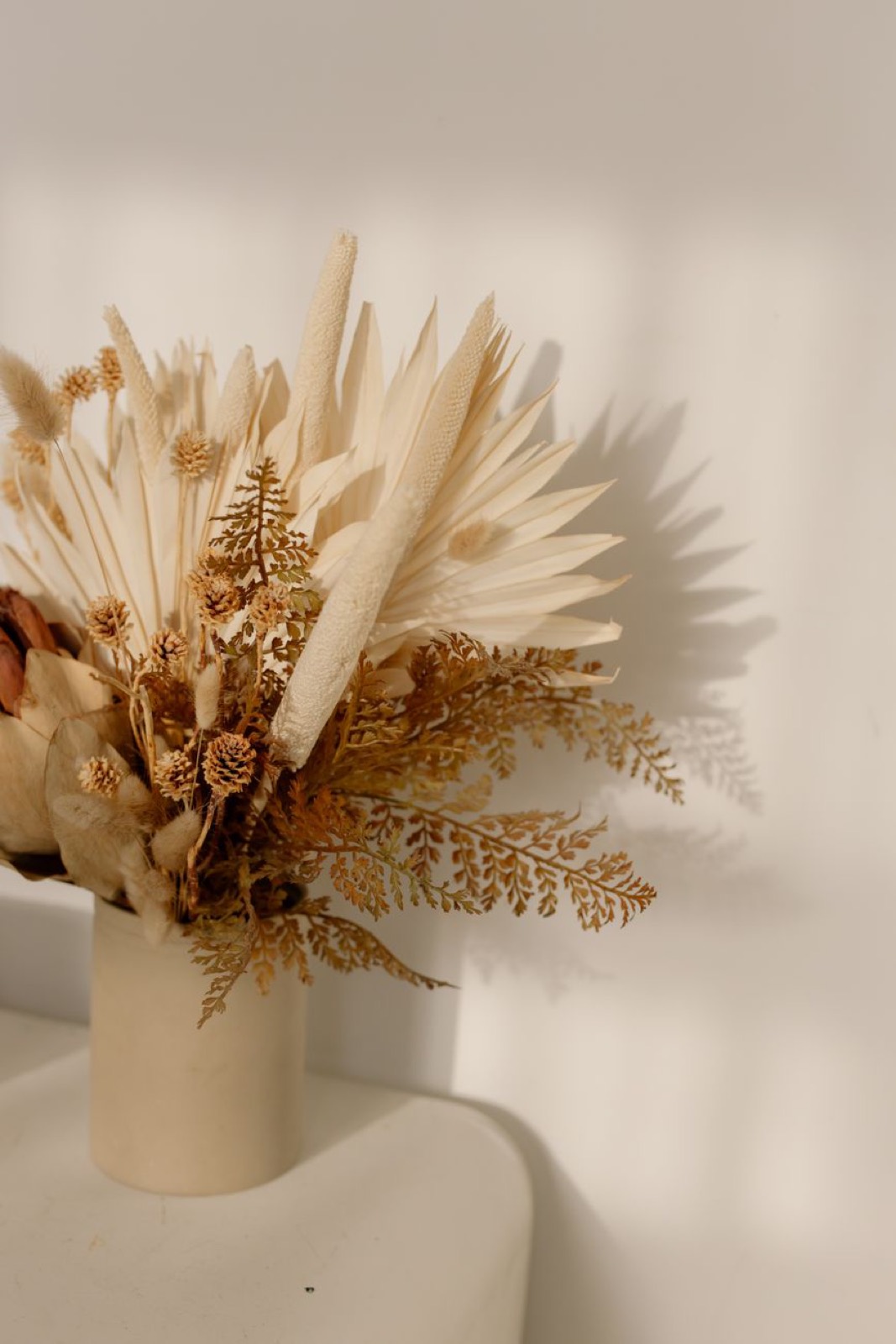 A bunch of dried palm and fern stems in a white vase