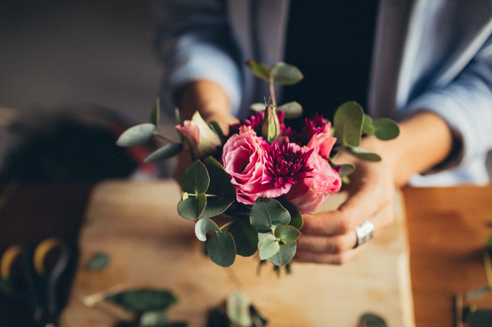 A florist's hands holding a bunch of pink roses and eucalyptus