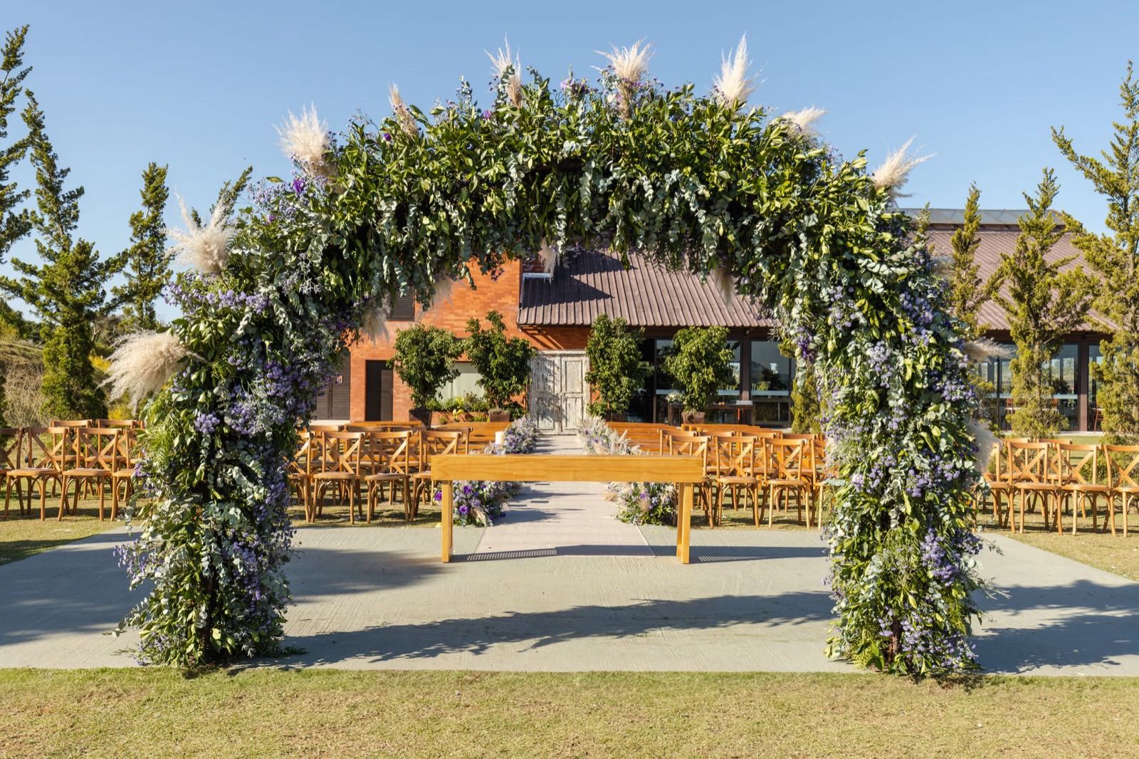 A flower arch of greenery and pampas at an outdoor wedding